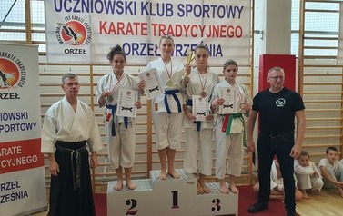 Aleksandra Arczewska i Dominik Oleksy stoją na podium z innymi zawodnikami. Obok stoją wręczający medale.