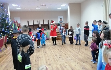 Dzieci w strojach karnawałowych stoją w k&oacute;łku, a Mikołajka objaśnia przez mikrofon zasady zabawy.