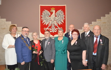 Pary pozują do zdjęcia z przedstawicielami władz samorządowych. W tle na ścianie godło Polski.