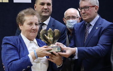 Członkowie kapituły konkursowej pozują z Panią Marią Głowacką do zdjęcia trzymając w rękach statuetkę