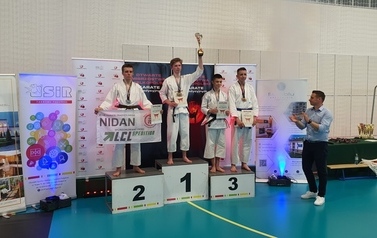 Czterech starszych zawodnik&oacute;w stoi na podium eksponując puchar za pierwsze miejsce oraz dyplomy. Obok stoi klaszcząc jeden z wręczających.