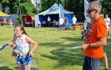 Dziewczynka z rakietą tenisową podczas konkursu sportowego. Obok stoi sędzi ze stoperem.