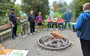 Wszyscy uczestnicy zajęć zgromadzeni wok&oacute;ł palącego się ogniska.