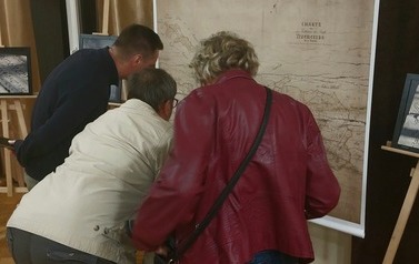 Trzy osoby pochyleni wpatrują się w kopię mapy Trzemeszna.