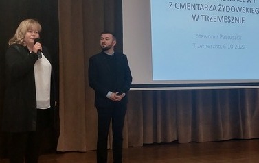Koordynatorka oraz wykładowca witają przybyłych gości, stojąc na scenie. W tle slajd z prezentacji.