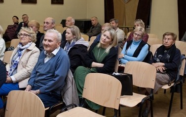 Widok na salę i siedzących na krzesłach, w rzędach widz&oacute;w.