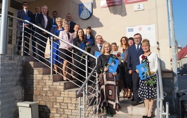 Nagrodzeni dyrektorzy na nauczyciele wraz z samorządowcami stoją na schodach urzędu i pozują do zdjęcia.