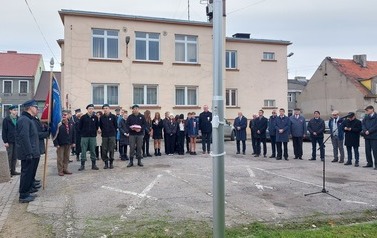 W p&oacute;łkolu wok&oacute;ł masztu stoją uczestnicy uroczystego podniesienia flagi narodowej.