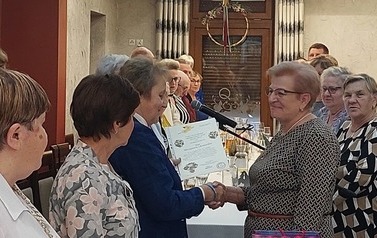 Wśr&oacute;d stojących członk&oacute;w prezes wręcza kolejne wyr&oacute;żnienie.