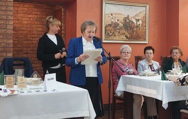 Prezes PSD w Trzemesznie stoi przy statywie z mikrofonem i odczytuje tekst z trzymanych w dłoniach kartek. Po prawej stronie przy stołach siedzą członkowie koła.