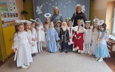 Dzieci w strojach z Jasełek pozują na stojąco do zdjęcia razem z dwoma paniami.