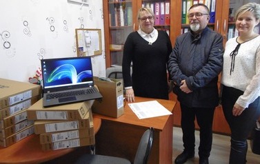 Na pierwszym planie stos karton&oacute;w z laptopami. Na g&oacute;rze jeden rozpakowany i otwarty. Za nimi stoją burmistrz, kierownik i dyrektor przedszkola nr 1.