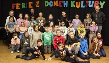 Dzieci z opiekunami pozują do zdjęcia. W tle napis Dom Kultury w Trzemesznie.