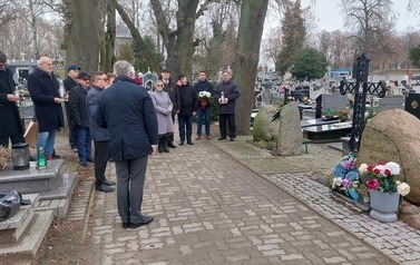 Uczestnicy spotkania stoją wok&oacute;ł obelisku, na cmentarzu.