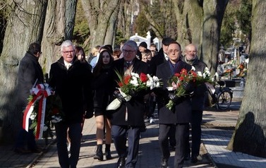 Widok na delegacje z kwiatami idące aleją przez cmentarz.