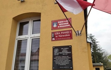 Tablice i flagi umieszczone na ścianie frontowej izby pamięci.
