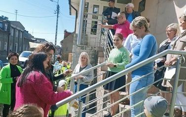 Grupa dzieci z opiekunami stoi przy schodach urzędu. Na schodach stoją urzędnicy.