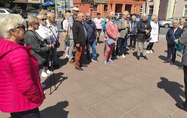 Grupa turyst&oacute;w z przewodnikiem stoi na skwerze Hipolita Cegielskiego.