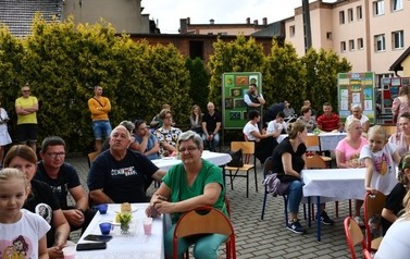 Rodzice i dzieci siedzą przy stolikach nakrytych białymi serwetkami.
