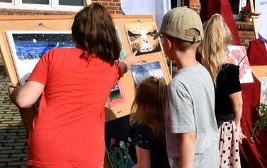 Uczniowie odwt&oacute;ceni tyłem do aparatu, podczas oglądania prac plastycznych wystawionych na sztalugach.