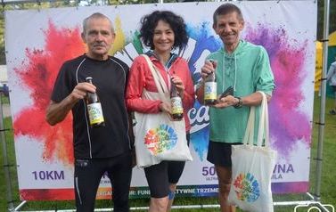 Kobieta i dw&oacute;ch mężczyzn pozują trzymając w rękach bitelki piwa. Na ramionach przewieszone pł&oacute;cienne torby z logo festiwalu.