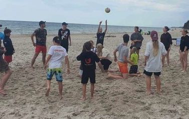 Młodzież podczas gry w piłkę siatkową na plaży. W tle morze.
