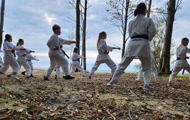 Zawodnicy w strojach karate ćwiczą w lesie nad brzegiem morza.