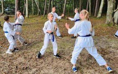 Zawodnicy w strojach karate ćwiczą w lesie.