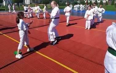 Zawodnicy w strojach karate ćwiczą na czerwonym korcie tenisowym.