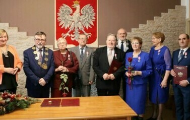 Trzy pary oraz wręczający medale pozują do zdjęcia na tle godła Polski