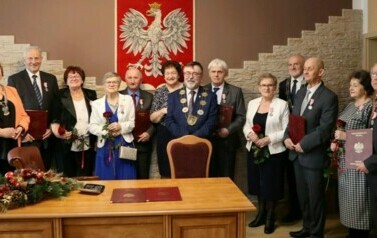 Pięć par oraz wręczający medale pozują do zdjęcia na tle godła Polski