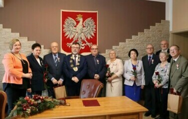 Cztery pary oraz wręczający medale pozują do zdjęcia na tle godła Polski