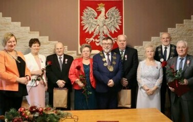 Trzy pary oraz wręczający medale pozują do zdjęcia na tle godła Polski