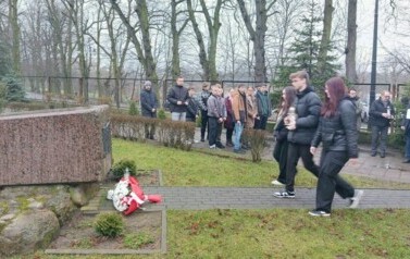 Do obelisku idzie delegacja uczni&oacute;w z wiązanką kwiat&oacute;w.