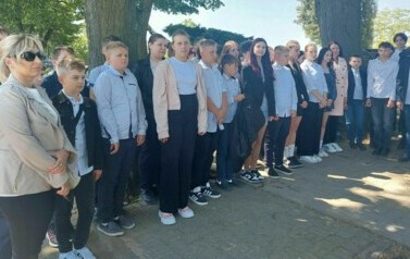 Grupa uczni&oacute;w i nauczycieli stoi w rzędzie w p&oacute;łokręgu.