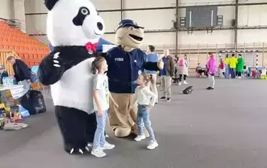 Hala sportowa. dwoje dzieci pozuje do zdjęcia z maskotkami: koali i policjanta. W tle stoiska i inne osoby.
