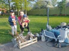 Mama zdw&oacute;jką dzieci, w tym jedno na rękach, pozują do zdjęcia. Przed nimi po lewej stronie w skrzyni sadzonki, a po prawej elektroodpady.