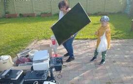 Kobeita i dziecko dokładają kolejne przedmioty do zgromadzonych elektroodpad&oacute;w.