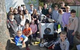 Grupa uczni&oacute;w pozuje stojąc dookoła elektroodpad&oacute;w.