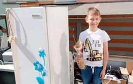 Chłopiec trzymając sadzonkę pozuje stojąc obok białej lod&oacute;wki.