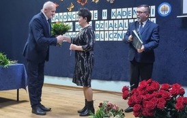 Na scenie przewodniczący rady miejskiej wręcza kwiaty wiceprzewodniczącej rady pożytku. Obok stoi burmistrz, kt&oacute;ry w rękach trzyma książkę.