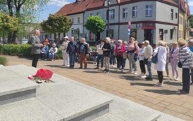 Grupa turyst&oacute;w z przewodnikiem stoi na placu Jana Kilińskiego. Z lewej strony widac schody od pomnika Kilińskiego.