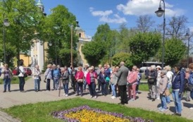 Grupa turyst&oacute;w z przewodnikiem stoi na placu Kosmowskiego. W tle bazylika.