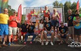 Trzy zawodniczki nordic walking z medalami na szyi stoją na podium. Wok&oacute;ł nich stoi i siedzi wielu innych zawodnik&oacute;w.