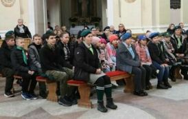 Grupa zuch&oacute;w i harcerzy w mundurach siedzi na ławkach w kościele.