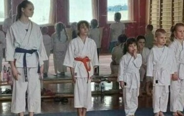 Zawodnicy w r&oacute;żnym wieku w strojach karate stoją na macie w rzędzie.