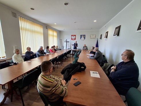 Sala urzędu. Przy stołach połączonych w podkowę siedzą członkowie komitetu.